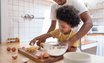 Happy Smiling african american Father helping his son kneading dough in kitchen, bake cookies.