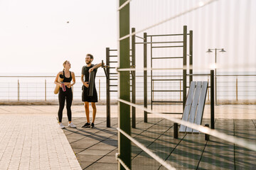 Young man and woman talking while working out together on sports ground