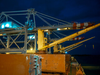 Fototapeta na wymiar Close up port crane unloading dry cargo ship at Industrial ship yard port at dawn at deep night. Marine shipping delivery