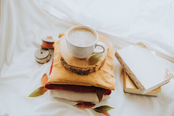 Tasse Kaffee auf einem Holzbrett auf bunten Pullovern mit Büchern nebendran und herbstlichen Blättern