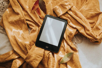 Modern e-book reader with blank screen on on an yellow autumn sweater, top view. Space for text