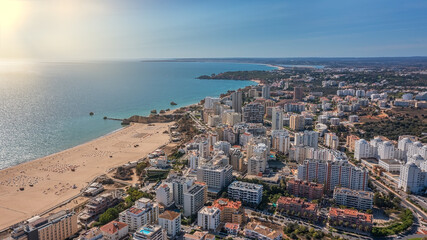 Fototapeta premium Aerial view of the city of Portimao over residential buildings, high-rise buildings, on the beach Praia de Rocha with tourists. Sunny day