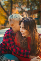 Boy son hugs his mother in red sweaters in the fall at the pond 