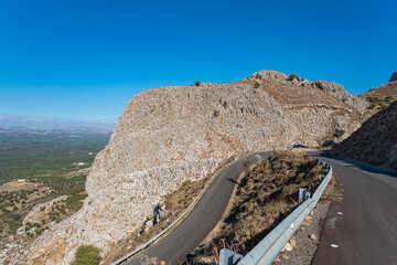 Huge rock at the hairpin turn on the way crossing the  Asterousia mountains  to Lentas. Scenic outlook to the great Messara plain in the south of Crete - obrazy, fototapety, plakaty