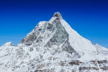 Scenic view on snowy Matterhorn peak in sunny day with blue sky and some clouds in background, Italy side