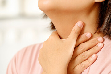 sore throat pain. Closeup of young woman sick holding her inflamed throat using hands to touch the ill neck in blue shirt on gray background. Medical and healthcare concept. Focus red on to show pain.
