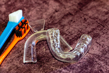 on a lilac background there is adental  mouth guard and two toothbrushes next to it; a silicone impression of teeth and an unused mold for the treatment of bruxism and against night snoring - obrazy, fototapety, plakaty