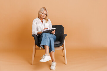 Mature blonde woman writing down notes while sitting in chair