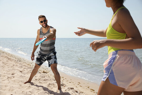 Couple playing with flying disk at beach on sunny day