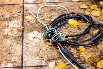 violation of rules and safety regulations; bare cables tied in a knot with protruding multicolored wiring lie on marble slabs in a puddle after rain in autumn