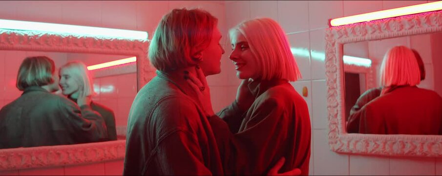 Waist up shot of sensual young couple kissing in old-fashioned bathroom filled with red neon light