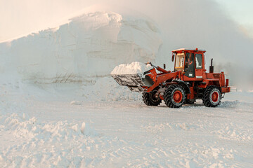 A bulldozer removes snow with a bucket after a blizzard. Cleaning snow drifts with a bulldozer.