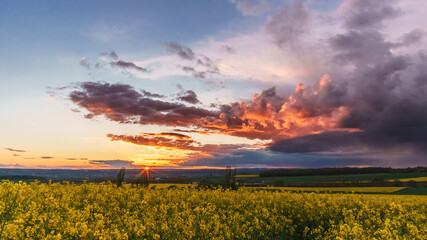 sunset with dramatic sky colorful with storm clouds over rural landscape with agricultural rape fields, Eifel, Germany