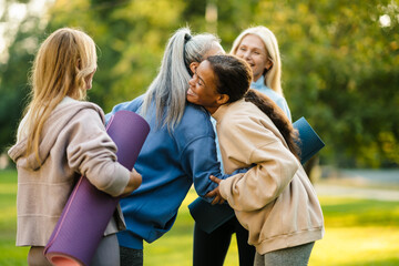 Multiracial women hugging and smiling after yoga practice in park