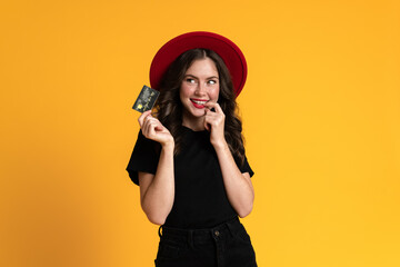 White young woman in red hat smiling while posing with credit card