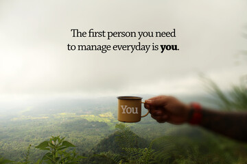 Inspirational motivational quote - The first person you need to manage everyday is you. Hand of person holding a cup of tea or coffee. On a gloomy sky background over the mountain in a misty morning.  - Powered by Adobe