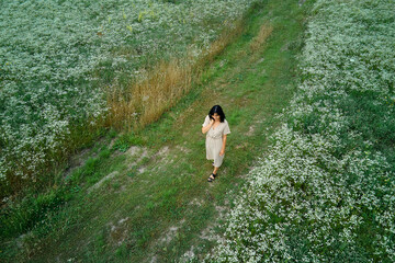 Drone aerial view of woman in dress walking in flower blooming meadow