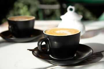 Two black ceramic cup of coffee on a marble table on an open terrace in bright sunlight