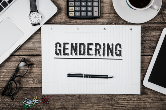 Wort Gendering als Titel auf einem Notizblock, der auf einem Tisch mit Büroutensilien und Technologie bestückt ist