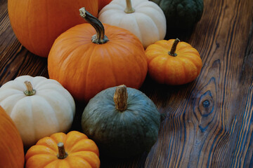 Bunch of pumpkins of different kinds, shapes and colors on wooden background as a symbol of autumnal holidays with a lot of copy space for text.