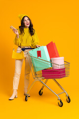 White excited woman posing with cellphone and shopping cart