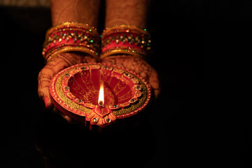 Beautiful Woman lady hand with bangles holding Eco Friendly Glowing Clay Diya Deep Dia lamps for Hindu festival Laxmi pooja or puja Diwali on a blck background