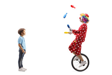 Full length shot of a boy standing and looking at a clown juggling on a unicycle