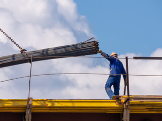 A worker holds a bundle of reinforcing bars while unloading. Lifting reinforcing bars on a building...