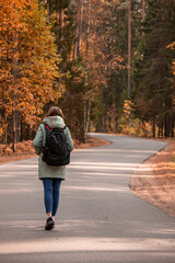 An unrecognizable female traveler enjoys a journey walking along a winding forest road.