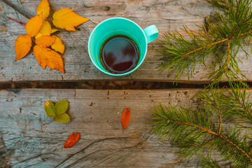 Mug with Tea, Top View, on a Wooden Background Among Pine Branches, Yellow Raspberry Leaves and Cones. Coffee on the Table in the Park. Picnic in the Nature. Autumn mood. 