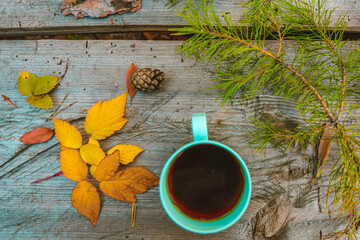 Mug with Tea, Top View, on a Wooden Background Among Pine Branches, Yellow Raspberry Leaves and Cones. Coffee on the Table in the Park. Picnic in the Nature. Autumn mood. 