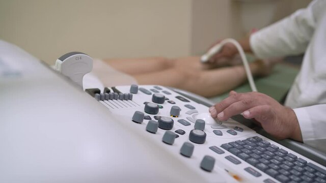 Doctor makes ultrasound of veins on patient's legs, close up. Phlebologist uses an ultrasound machine to scan a patient. The doctor checks the veins in the patient's legs with a machine.
