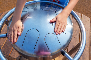 Child's hands playing Hang pan Drum outdoors. Zen-like modern trendy musical instrument.