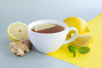 Tea with lemon and ginger in the white cup on the gray  yellow background. Close-up.