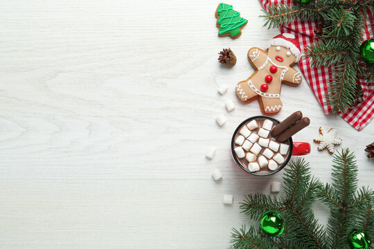 Delicious hot chocolate with marshmallows and cocoa sticks near Christmas decor on white wooden table, flat lay. Space for text