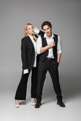 full length view of stylish couple in elegant clothes looking at camera on grey