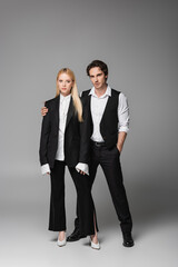 stylish man standing with hand in pocket near blonde woman on grey