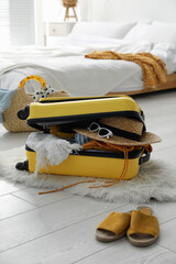 Open suitcase full of clothes, shoes and summer accessories on floor in room