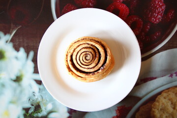 Appetizing cinnamon roll on a white plate, top view