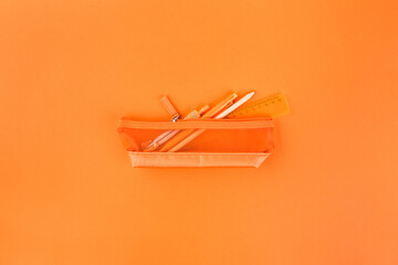 Different orange school supplies in case on orange table. Back to school concept. Flat lay, top view. Orange rush.