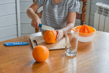 the child girl in the kitchen cuts and squeezes oranges juice