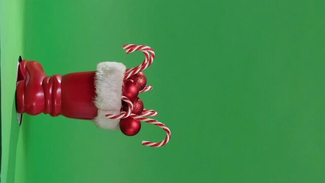 4K. Vertical video Christmas Scene with Red boot of Santa Claus. Christmas boot stocking with gifts on a green background. Red Santa's boot with copyspace. Santa Claus boot stuffed with presents