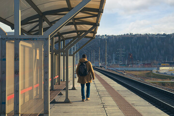 A young man with a backpack walks along the platform of the railway station. Railway transport, travel, communications.