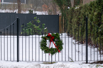 A green evergreen branch wreath with a bright red bow attached to a black iron gate enclosing a...