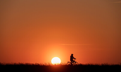 Obraz na płótnie Canvas Silhouette of man on bike on grass on sunset with back lite and sun on backgound