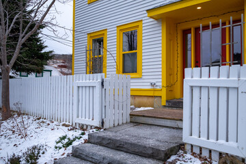 The corner of a white clapboard wood house with multiple double hung windows with vibrant yellow...