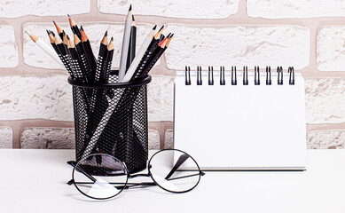Workplace in the house with glasses, pencils in a stand and a blank notebook with a place to insert...
