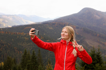 Naklejka na ściany i meble Happy young woman taking selfie with phone in mountains
