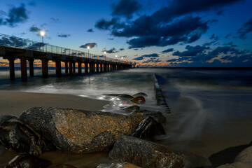 Pier in the sea at night, rocky beach in the foreground