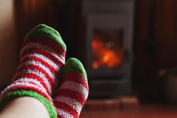 Feet legs in winter clothes wool socks at fireplace background. Woman sitting at home on winter or autumn evening relaxing and warming up. Winter and cold weather concept. Hygge Christmas eve.